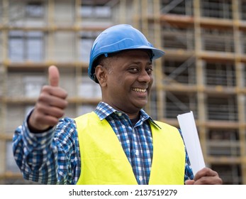 Portrait Of A Positive And Successful Indian Engineer Holding Rolled Up Plans, Smiling At The Camera And Showing A Thumbs Up Gesture