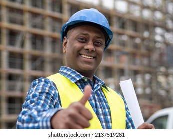 Portrait Of A Positive And Successful Indian Engineer Holding Rolled Up Plans, Smiling At The Camera And Showing A Thumbs Up Gesture