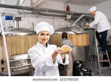 Portrait of positive woman brewmaster holding bunch of hops pellets in beer factory. - Powered by Shutterstock