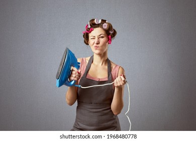 Portrait of positive woman hold metal iron wear hair rollers and apron isolated gray background.Funny housewife doing household chores and ironing clothes.