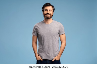 Portrait of positive young bearded man in t shirt posing in studio, looking at camera, isolated on blue background. Advertisement concept - Powered by Shutterstock