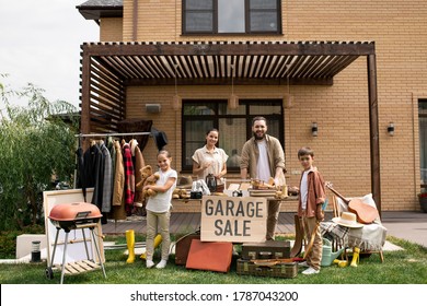 Portrait Of Positive Young Family With Two Kids Waiting For Customers At Garage Sale