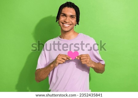 Portrait of positive young man beaming smile arms hold little heart symbol card isolated on green color background