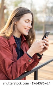 Portrait Of Positive Young Woman Chatting On Her Mobile Phone With A Big Smile On Her Face With A Beautiful Brunette Hair Outside 