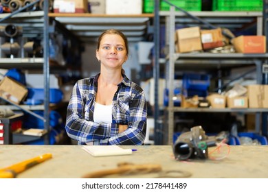 Portrait Of Positive Young Woman Warehouse Worker Standing At Workbench.