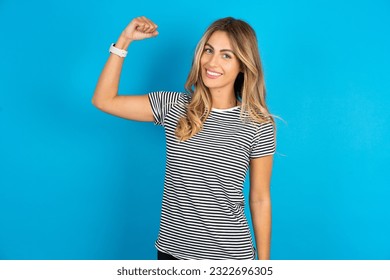 Portrait of powerful cheerful Young beautiful woman wearing striped t-shirt  showing muscles.