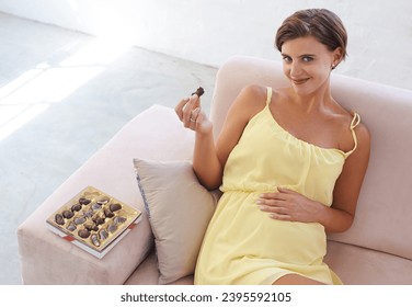 Portrait, pregnant woman and eating chocolate in home, alone and happiness for delicious pregnancy craving. Good mood, comfort food and candy dessert for maternity, snack and sweet tooth satisfaction - Powered by Shutterstock