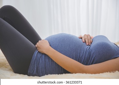 A portrait of pregnant woman laying on a bed, close up on the stomach