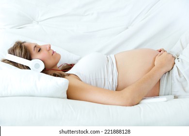 Portrait of pregnant woman sitting on sofa at home and listening music in headphones. - Powered by Shutterstock