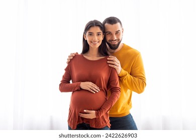 Portrait Of Pregnant Young Woman And Her Husband Embracing Near Window At Home, Expectant Caucasian Spouses Smiling At Camera, Enjoying Future Parenthood, Getting Ready To Be Parents, Copy Space - Powered by Shutterstock