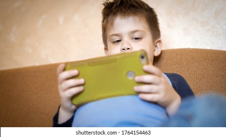 Portrait Of Preschool Child Holding Father's Mobile Phone Looking On It. Close Up Shot From Below.