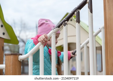 Portrait Of A Preschool Child On The Playground. A Five-year-old Girl In A Pink Hat Walks Up And Down The Stairs Holding Onto The Railing. Childhood. View From The Bottom Up.