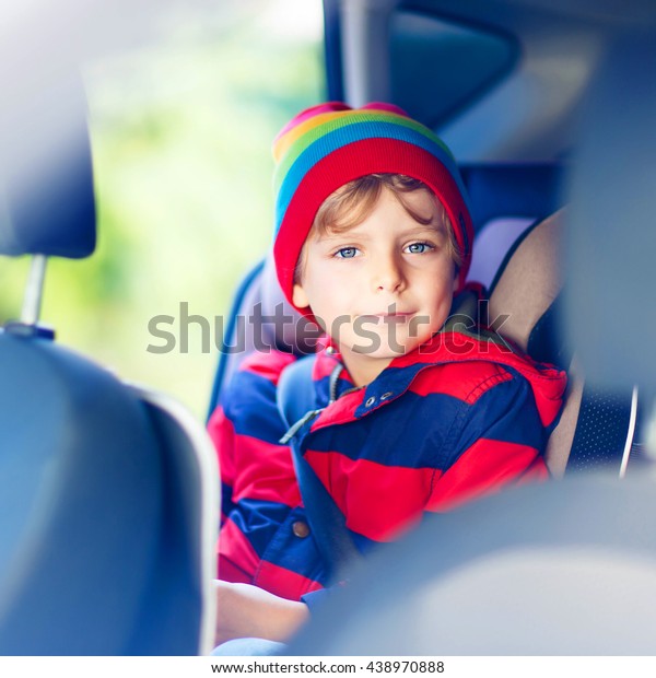 Portrait of preschool little kid boy sitting in\
car. Child in safety car seat with belt. Safe travel with kids and\
traffic laws concept.