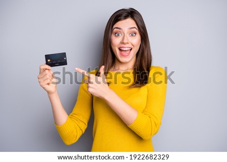 Portrait of pretty amazed glad cheerful girl holding in hands demonstrating bank card novelty isolated over grey color background