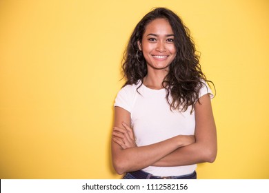 portrait of pretty asian girl smiling with arm crossed on yellow background
