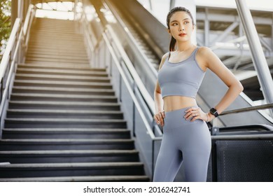 Portrait of pretty asian woman Standing on floor of city street after running. Female athlete runner resting, workout outdoors on fresh air, jogger take break, wearing sports outfit.