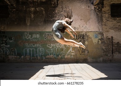 Portrait of a pretty ballet dancer in the air while performing a dance routine outdoors in front of a graffiti wall - Powered by Shutterstock