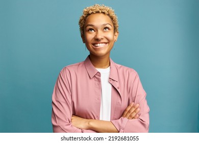 Portrait of pretty black girl of 20s looking up smiling biting lips, planning something, remembering funny moments, thinking about her boyfriend, standing with crossed hands on blue background - Shutterstock ID 2192681055