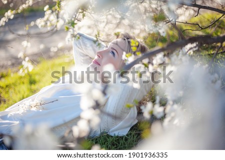 Portrait of pretty blond girl posing against the spring flowers. Woman enjoy the healthy aroma smelling in the garden