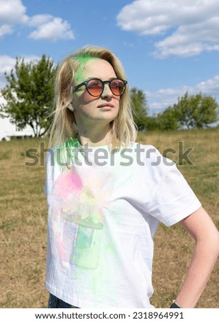 Portrait Pretty Blond Woman With Colored Dye, Powder On Face And Cloth On Holi Colors Festival In Meadow, Sunny Day. Playful Cultural Event With Throwing Bright Neon Powder. Vertical Plane.
