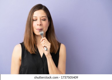 Portrait of a pretty brunette woman enjoying some delicious food with a fork in a studio and her eyes closed