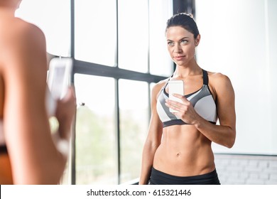 Portrait Of Pretty Brunette Woman Smiling Taking Mirror Selfie In Gym,  Posing Boasting Her Fit Figure And Slim Waist