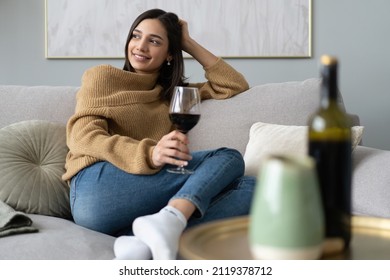 Portrait of pretty, charming, attractive, stylish young woman sitting on couch having raised glass with red wine in hand, examine, taste beverage - Powered by Shutterstock