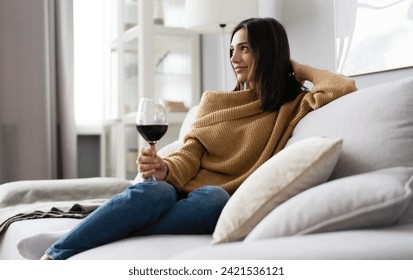 Portrait of pretty, charming, attractive, stylish woman sitting on couch having raised glass with red wine in hand, examine, taste beverage - Powered by Shutterstock