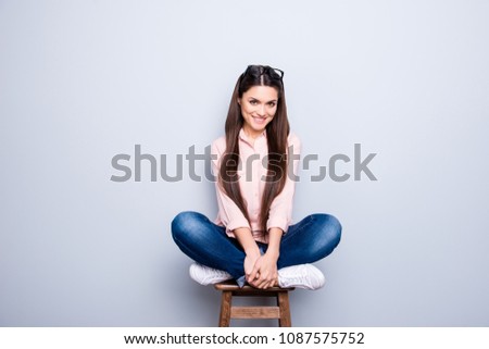 Portrait of pretty charming funny cheerful positive cute woman with glasses on head long hair sitting on wooden bar chair with crossed legs looking at camera isolated on grey background