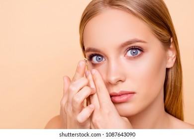 Portrait Of Pretty, Charming, Nude, Natural Girl Putting Crystalline Lens In Right Eye With Forefinger Looking At Camera Isolated On Beige Background