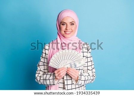 Portrait of pretty cheerful muslimah girl holding in hands budget finance isolated over bright blue color background