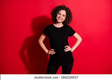 Portrait of pretty cheerful wavy-haired girl posing hands on hips wearing black look isolated over bright red color background