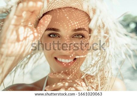 Portrait of pretty cheerful woman wearing straw hat in sunny warm weather day. Walking on the beach