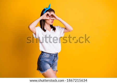 Portrait of pretty cheery flirty brown-haired girl showing looking through heart shape sending air kiss isolated on bright yellow color background