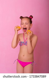 Portrait of pretty child holding slices of lemon. Girl playing with lemon. Little girl eating lemon isolated on pink background, grimacing. Girl shows tongue, has fun.