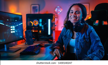 Portrait of a Pretty and Excited Black Gamer Girl in Headphones who Finished Playing Video Game on Her Computer. She Turn and Smiles into the Camera. Home is Lit with Neon Lights.