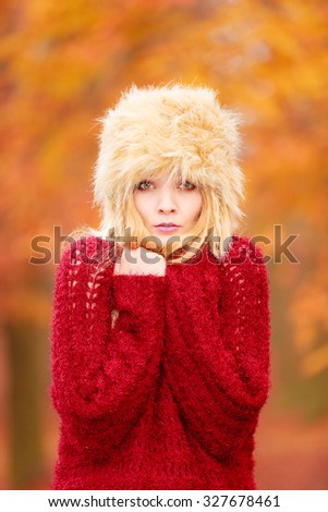 Portrait of pretty fashionable woman in fall forest park feeling cold. Gorgeous young girl in fur winter hat and sweater shivering. Autumn fashion.