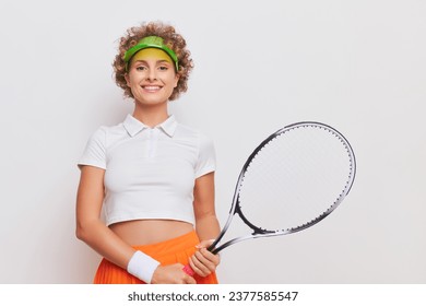 Portrait of pretty female tennis player from waist up with tennis racket in her hands, smiling and looking at camera, sport life concept, copy space. - Powered by Shutterstock