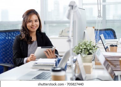 Portrait of pretty Filipino business woman sitting at her table with tablet computer