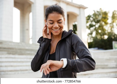 Portrait of a pretty fitness woman in earphones checking her smart watch outdoors - Powered by Shutterstock