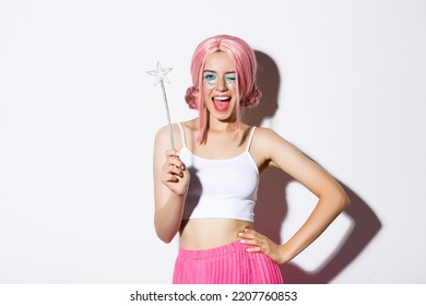 Portrait of pretty girl celebrating halloween in fairy costume, wearing pink wig and bright makeup, holding magic want and smiling, standing over white background - Powered by Shutterstock