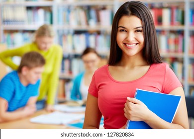 Portrait Of Pretty Girl Looking At Camera In College Library With Her Group Mates On Background