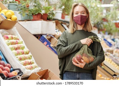 Portrait Of Pretty Girl In Mask Holding Net Bag Of Organic Products At Farmers Market During Coronavirus