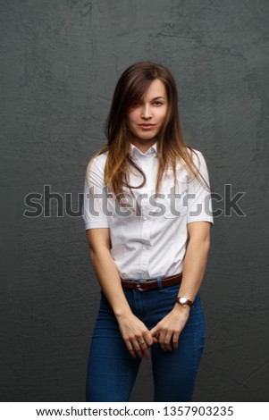 Portrait of pretty girl in strict casual clothes with tousled hair against the background of a gray wall.