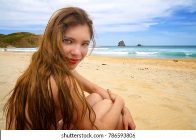 Portrait of pretty happy girl with the perfect fit body at the wild Pacific ocean coast, nude sunbathing woman at Otago Peninsula's Sandfly Bay clothing optional sandy beach, New Zealand