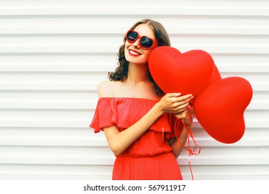 Portrait pretty happy smiling woman in red dress and sunglasses with air balloons heart shape over white background