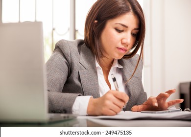 Portrait of a pretty Hispanic accountant in a suit doing some calculations with the help of a smart phone