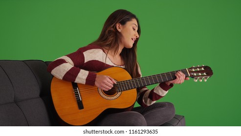 Portrait of pretty Hispanic woman playing guitar and singing on green screen - Powered by Shutterstock