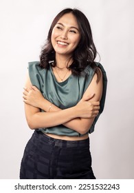 Portrait of a pretty Indonesian Asian girl in her 20s, wearing a light grey top and black trousers, smiling as her hugging herself. Isolated on white background.