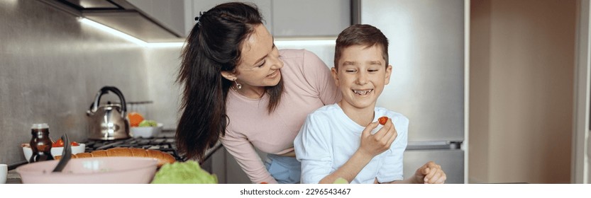 Portrait of pretty joyful mother smiling and looking at cute son eating cherry tomato. - Powered by Shutterstock